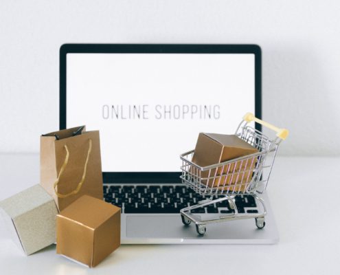 En laptop med texten "online shopping" på skärmen, små paket, en liten kundvagn och kasse står på tangentbordet